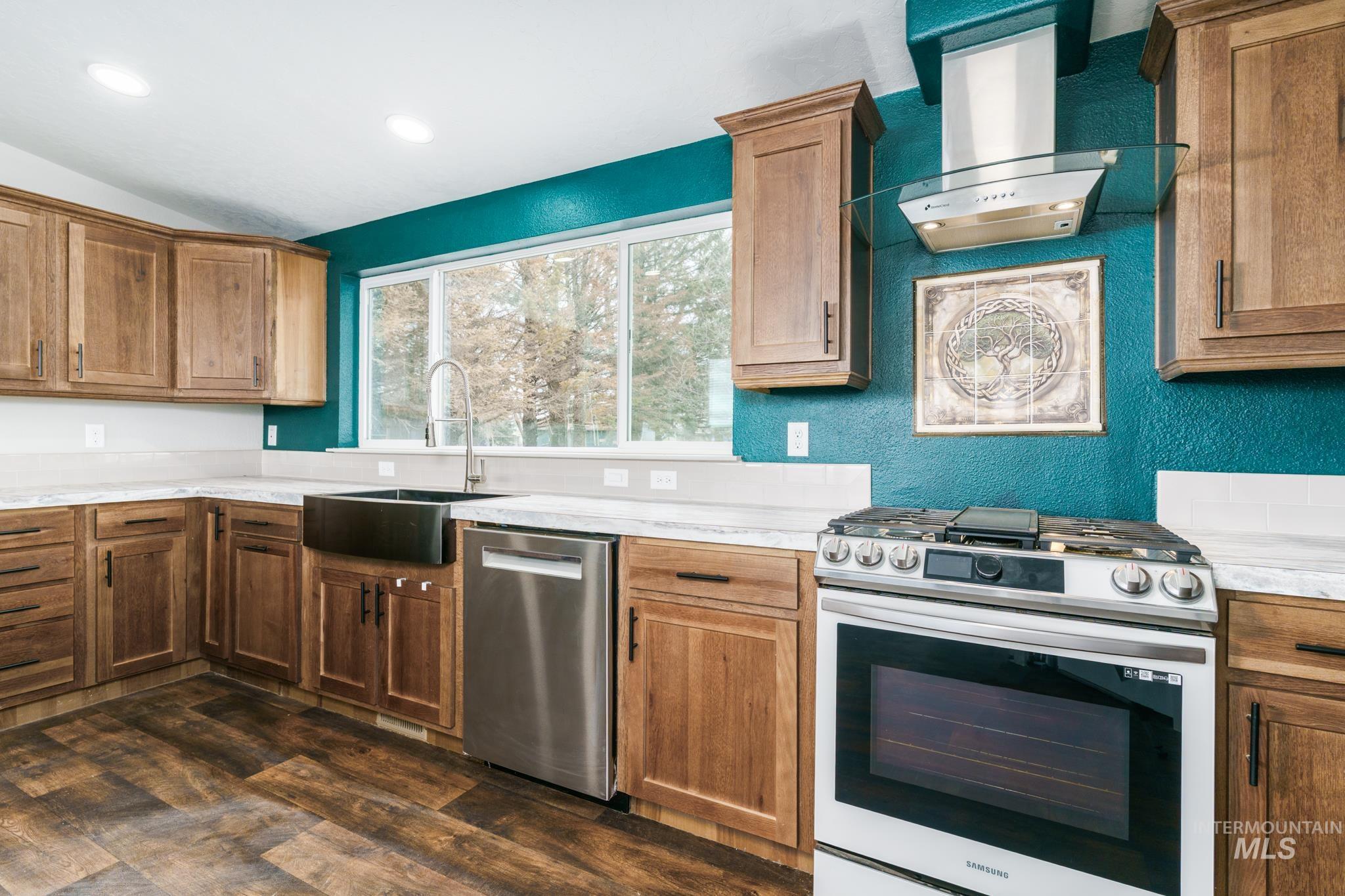 13678 North Hawthorne Road Pocatello, ID 83202 - Photo 5 of 37 Kitchen featuring appliances with stainless steel finishes, wall chimney exhaust hood, a textured wall, brown cabinets, and vaulted ceiling