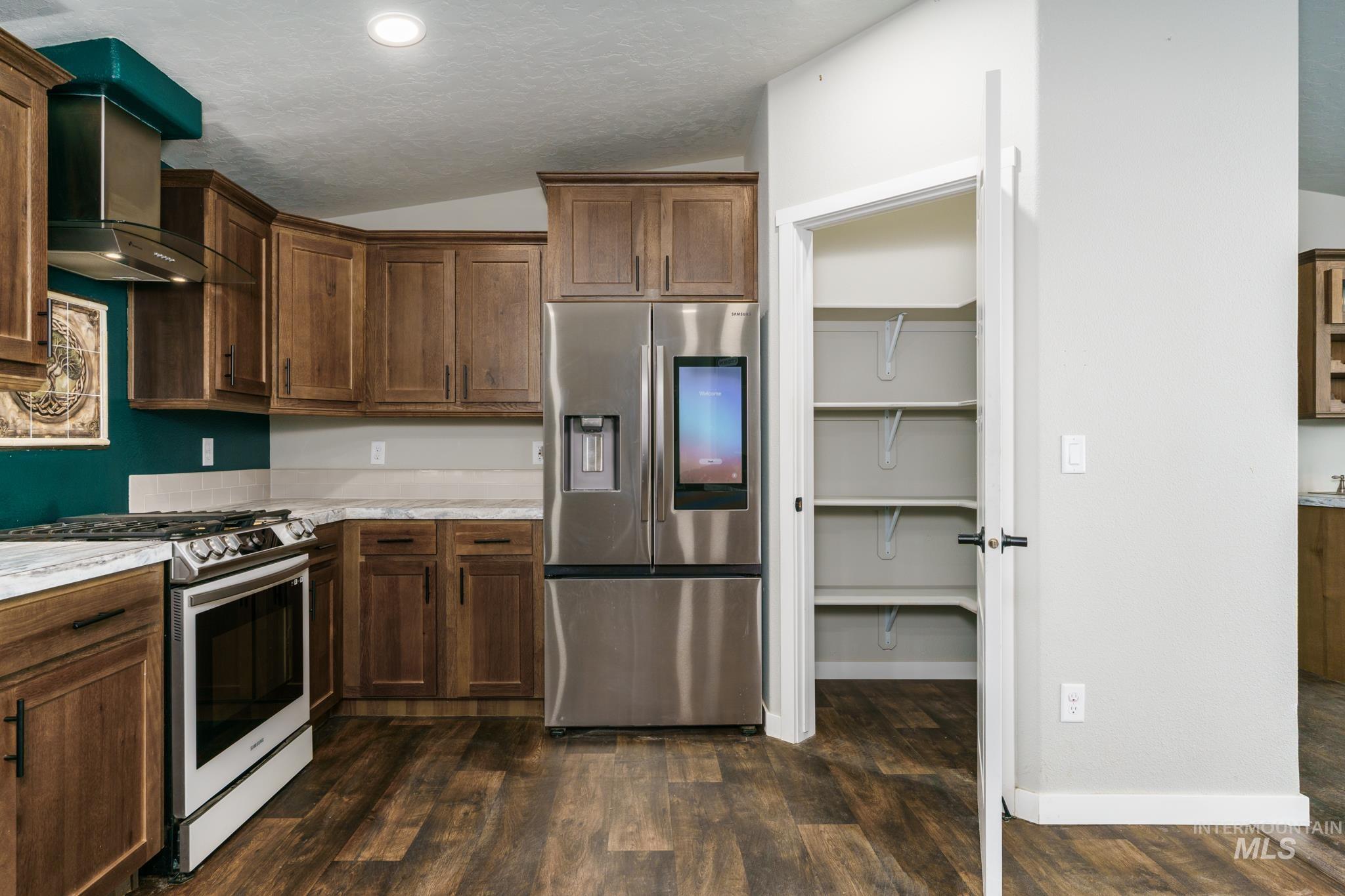 13678 North Hawthorne Road Pocatello, ID 83202 - Photo 7 of 37 Kitchen featuring vaulted ceiling, appliances with stainless steel finishes, wall chimney exhaust hood, dark wood-style floors, and dark brown cabinets