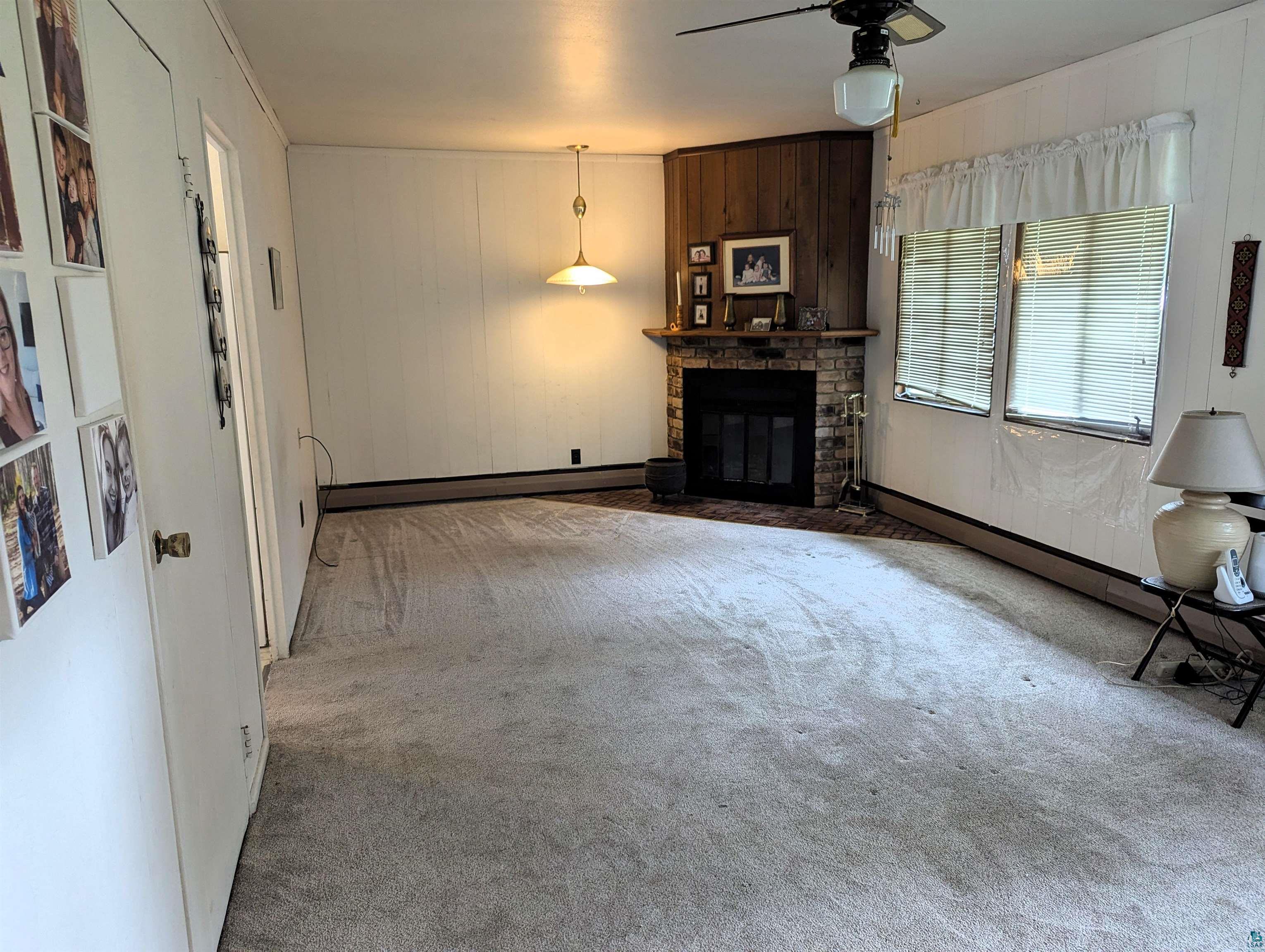 28 James Road Silver Bay, MN 55614 - Photo 16 of 37 Unfurnished living room featuring carpet floors, ceiling fan, a baseboard radiator, and a brick fireplace