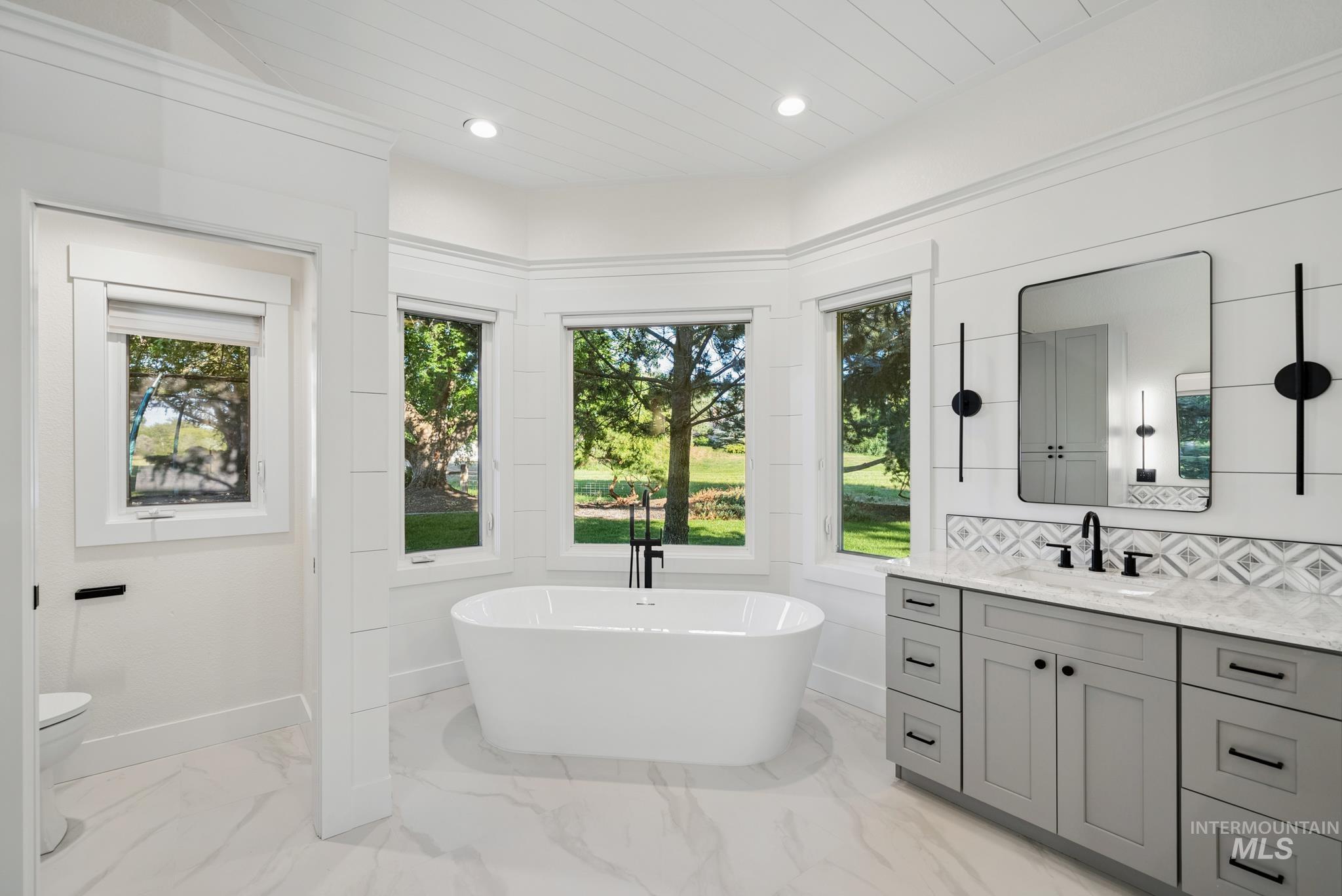 2050 Artesian Road Eagle, ID 83616 - Photo 26 of 49 Spacious bathroom featuring a freestanding soaking tub, a large walk-in shower with a glass enclosure, dual vanities with quartz countertops, a vanity desk area, and plank-style ceiling details