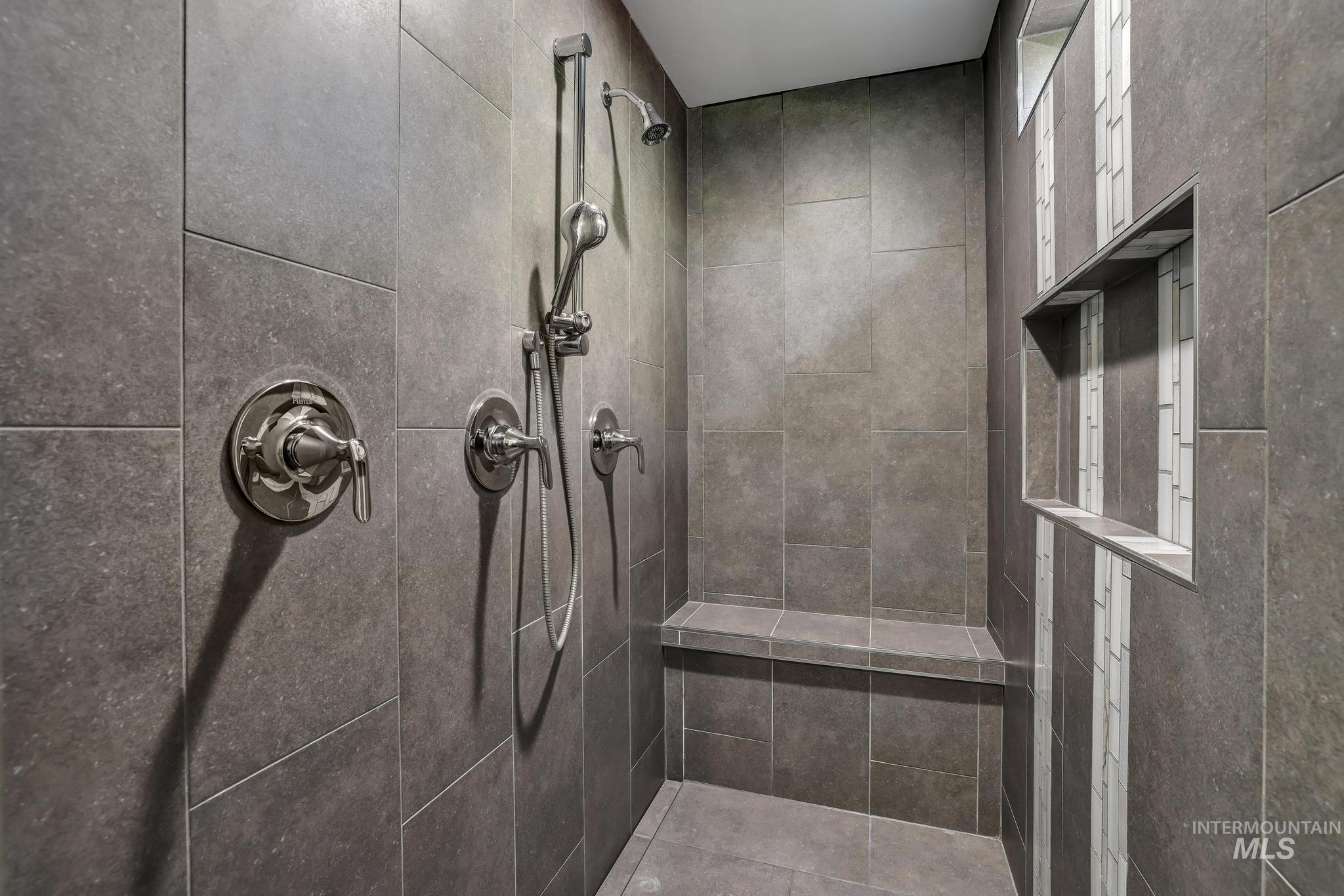 1937 Tamarack Loop Twin Falls, ID 83301 - Photo 35 of 50 Spacious shower enclosure featuring large format grey tile, a built-in bench, two recessed niches with contrasting tile accents, a fixed shower head, and a handheld shower wand