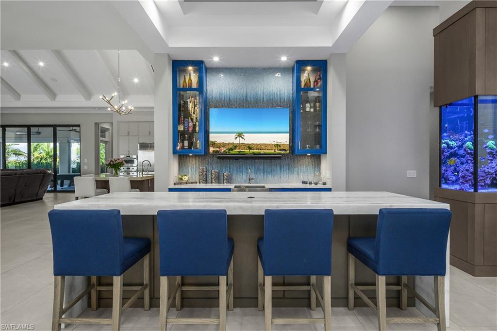 18410 Blue Eye Loop Fort Myers, FL 33913 - Photo 14 of 49 The social bar and gathering space is an entertainer's delight and blends aesthetic appeal with practical function, featuring waterfall leathered quartz countertops, glass ombre custom tile backsplash, glass door cabinetry, beverage cooler, & ice maker.