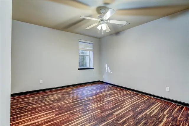 an empty room with wooden floor chandelier fan and windows