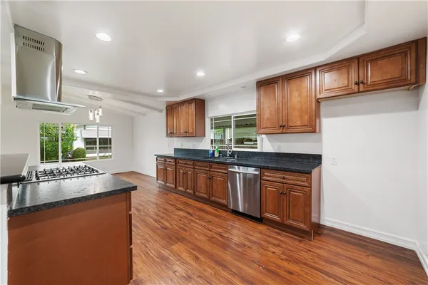 a kitchen with stainless steel appliances granite countertop wooden cabinets a refrigerator a sink a stove a microwave and wooden floors