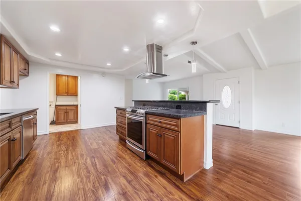 a kitchen with stainless steel appliances granite countertop wooden cabinets a stove top oven and a wooden floor