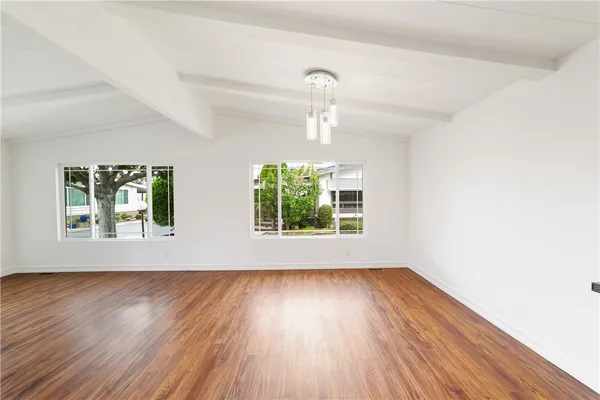 an empty room with wooden floor chandelier fan and windows
