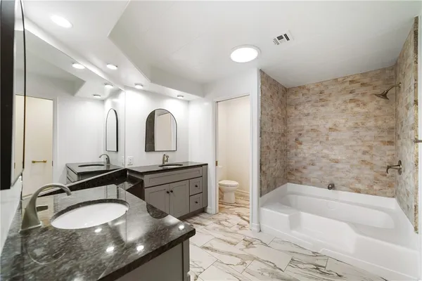 a bathroom with a granite countertop double vanity sink and a bathtub