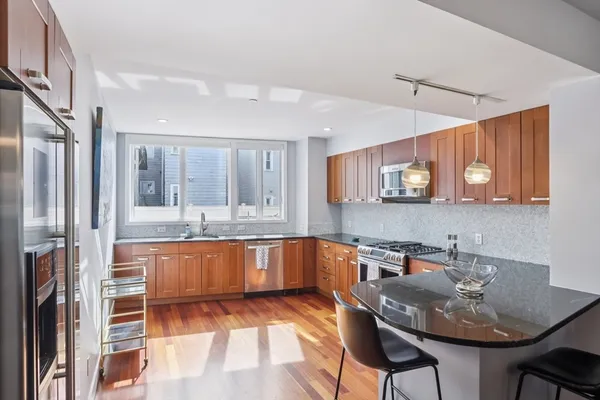 a kitchen with stainless steel appliances granite countertop a stove top oven a sink dishwasher a dining table and chairs with wooden floor