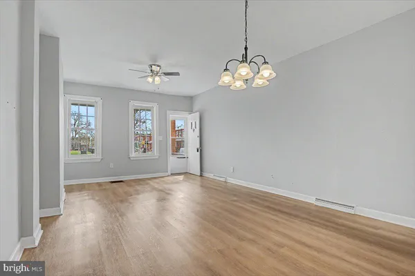 an empty room with wooden floor chandelier fan and windows