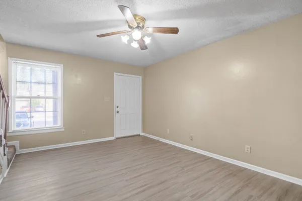 an empty room with wooden floor chandelier fan and windows
