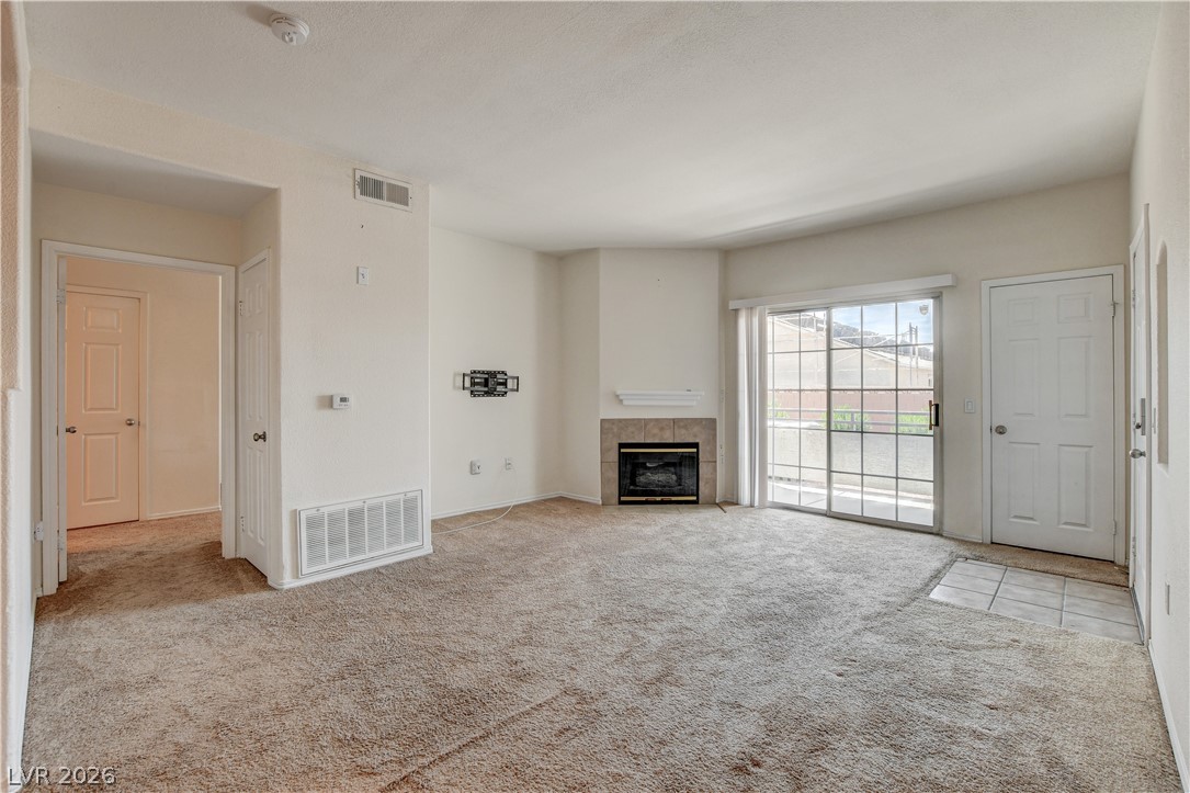 3318 North Decatur Boulevard, Unit 1069 Las Vegas, NV 89130 - Photo 4 of 39 A cozy living space features a corner fireplace with a tiled hearth and direct access to an outdoor area through sliding glass doors.