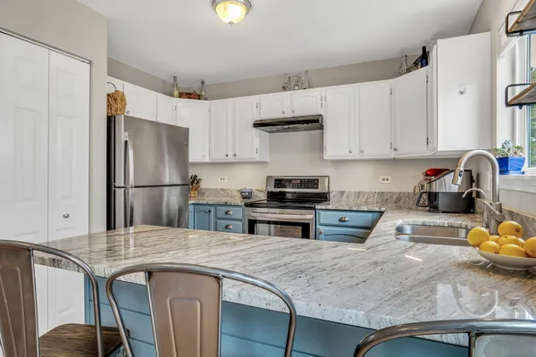 a kitchen with stainless steel appliances a stove a sink a refrigerator white cabinets and chairs