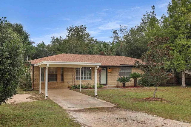 a view of a white house with a yard plants and large tree