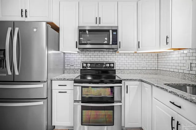 a kitchen with granite countertop white cabinets and stainless steel appliances
