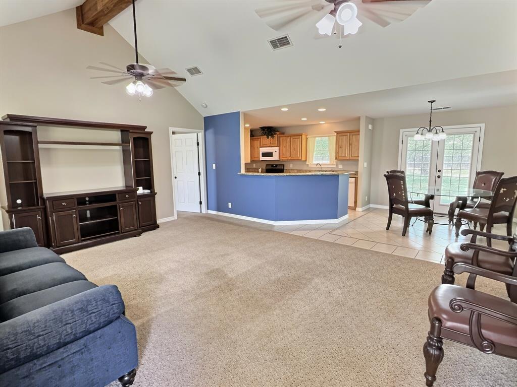 313 East River Oaks Road Early, TX 76802 - Photo 5 of 34 Vaulted ceiling with exposed wood beam, kitchen with wood cabinetry and stone countertops, tiled dining area, and French patio doors