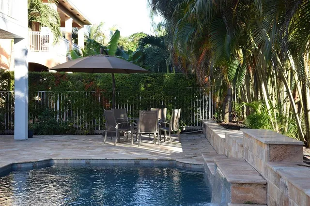 a view of a patio with table and chairs under an umbrella with large trees