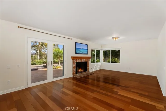 a view of an empty room with wooden floor fireplace and a window