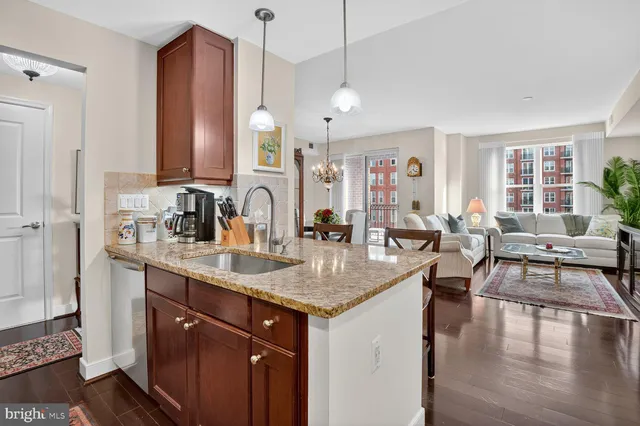 a view of center island of a kitchen with granite countertop a sink a counter top space and living room view