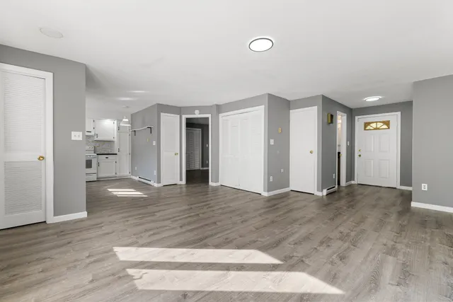 a view of an empty room with wooden floor and a kitchen