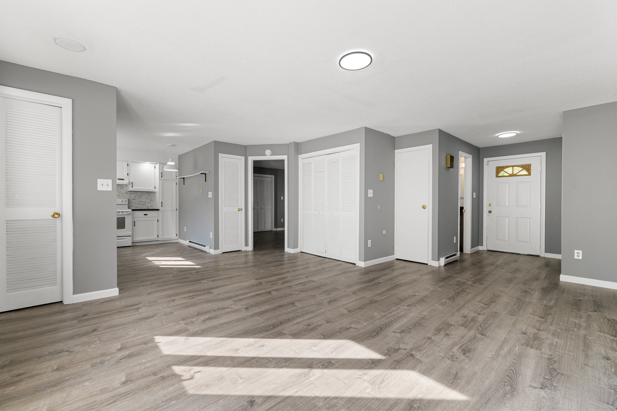 a view of an empty room with wooden floor and a kitchen