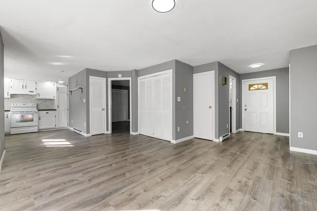 a view of an empty room with wooden floor and a kitchen