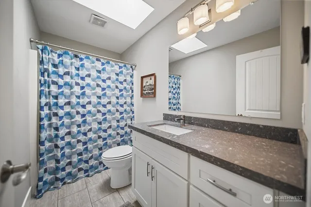 a bathroom with a granite countertop toilet a sink a mirror a window and a shower