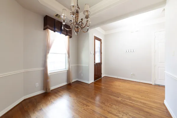 an empty room with wooden floor chandelier and windows