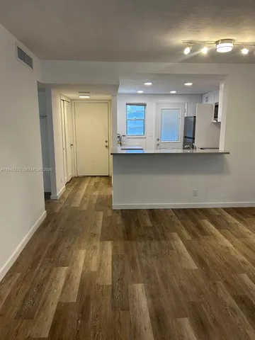 an empty room with wooden floor and kitchen view