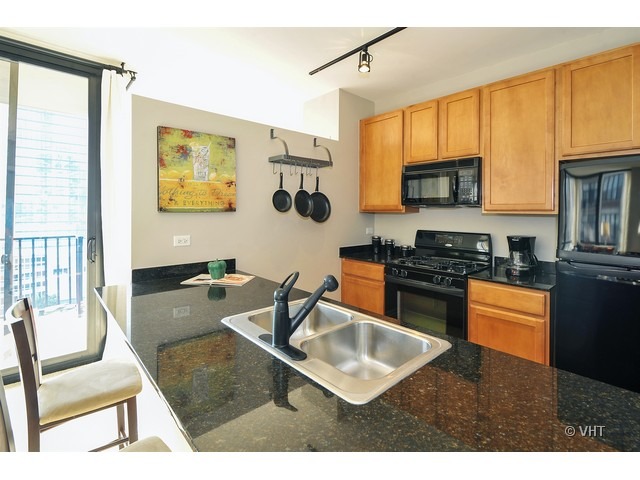210 South Desplaines Street, Unit 910 Chicago, IL 60661 - Photo 4 of 12 a kitchen with stainless steel appliances granite countertop a stove top oven a sink a dining table and chairs with wooden floor