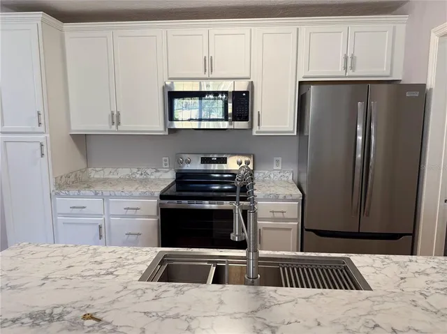 a kitchen with granite countertop a refrigerator stove and white cabinets
