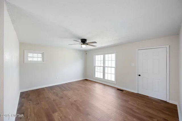 an empty room with wooden floor chandelier fan and windows