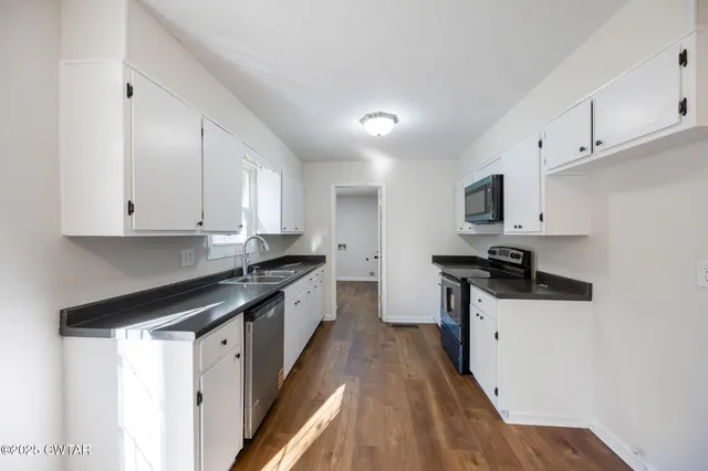 a kitchen with granite countertop a sink a stove top oven and white cabinets