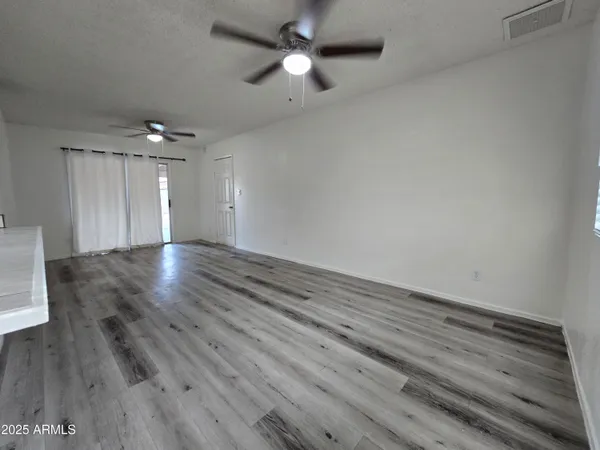 an empty room with wooden floor ceiling fan and window