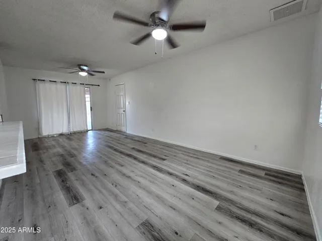 an empty room with wooden floor ceiling fan and window