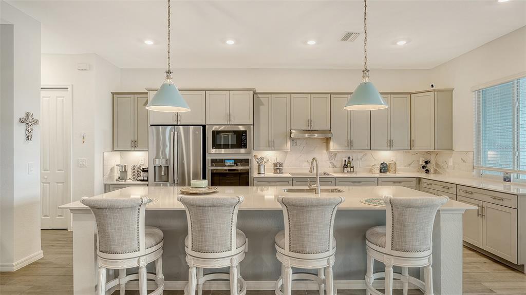12716 Tulum Loop Venice, FL 34293 - Photo 9 of 97 a kitchen with stainless steel appliances kitchen island granite countertop a table chairs refrigerator and microwave