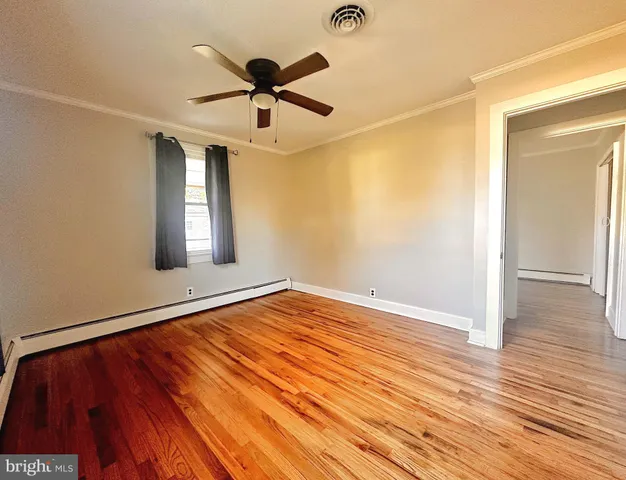 a view of empty room with wooden floor and fan