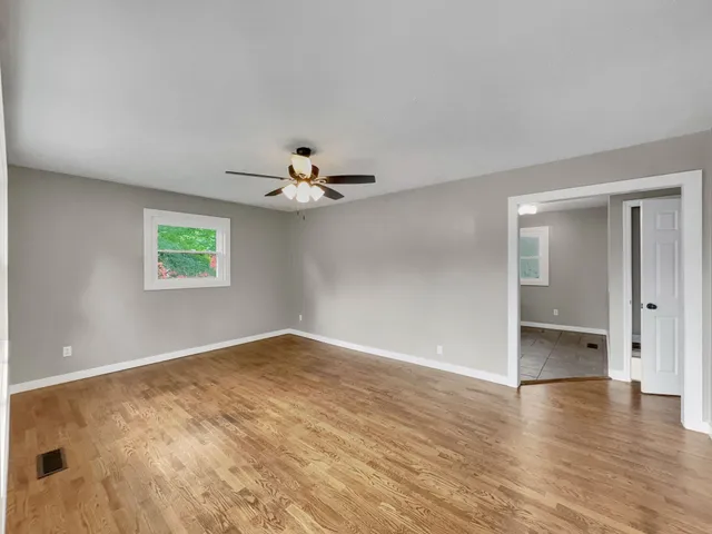 an empty room with wooden floor chandelier fan and windows