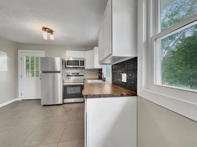 a kitchen with granite countertop a refrigerator oven a sink dishwasher and white cabinets next to a window