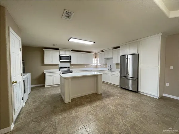 an empty room with kitchen and chandelier fan