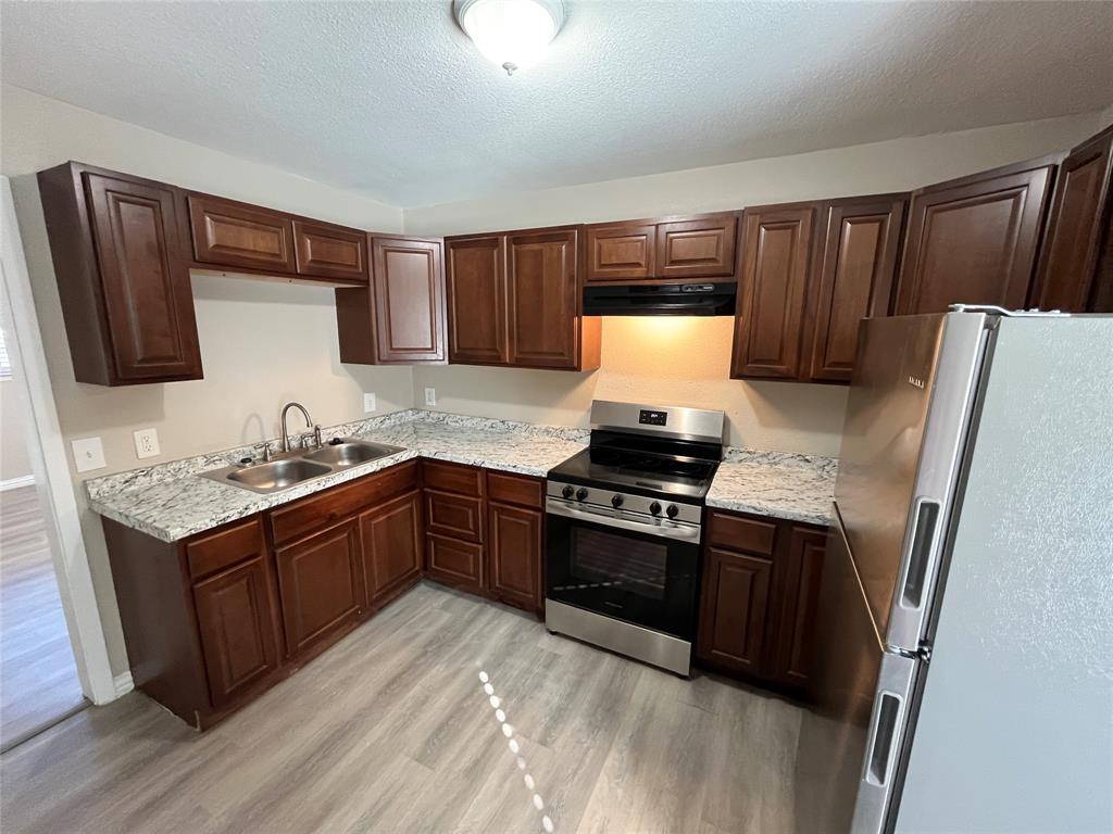 8335 Tenino Street Dallas, TX 75217 - Photo 6 of 22 Kitchen featuring appliances with stainless steel finishes, light wood finished floors, a textured ceiling, dark brown cabinetry, and under cabinet range hood