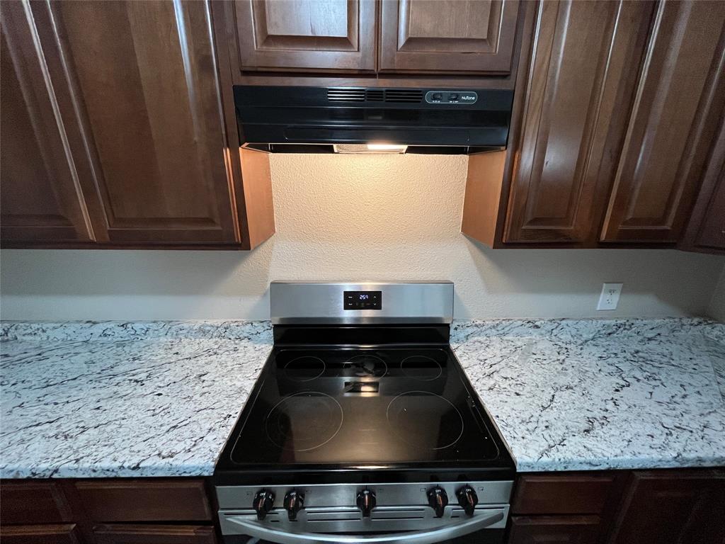 8335 Tenino Street Dallas, TX 75217 - Photo 7 of 22 Kitchen with dark brown cabinets, stainless steel range with electric cooktop, under cabinet range hood, light stone countertops, and a textured wall
