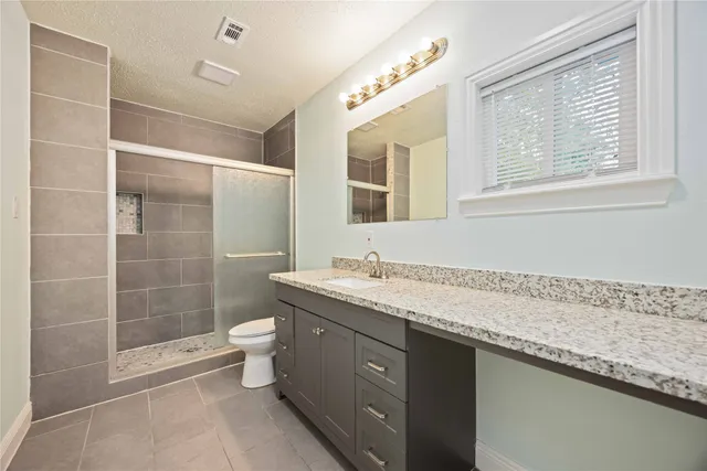 a bathroom with a granite countertop sink a toilet a mirror and shower