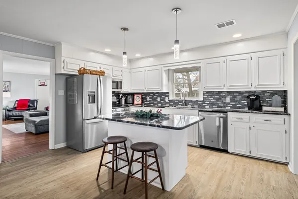 a kitchen with stainless steel appliances granite countertop a refrigerator a sink dishwasher a stove and white cabinets with wooden floor