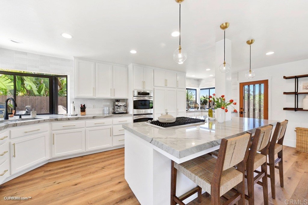 3815 Trieste Drive Carlsbad, CA 92010 - Photo 7 of 24 a kitchen with stainless steel appliances granite countertop a stove a sink a kitchen island with chairs and wooden floor