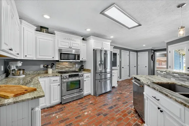 a kitchen with granite countertop a stove a sink a refrigerator and white cabinets with wooden floor