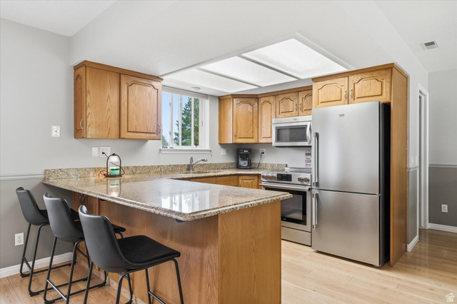 45 West 100 South Mendon, UT 84325 - Photo 15 of 64 Kitchen featuring stainless steel appliances, light stone counters, light wood-type flooring, a peninsula, and a breakfast bar