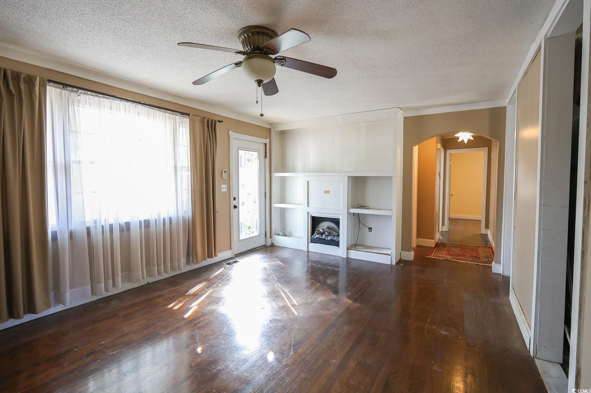 1841 Jasper Street Georgetown, SC 29440 - Photo 13 of 33 Unfurnished living room featuring ornamental molding, a healthy amount of sunlight, dark hardwood / wood-style flooring, and a textured ceiling