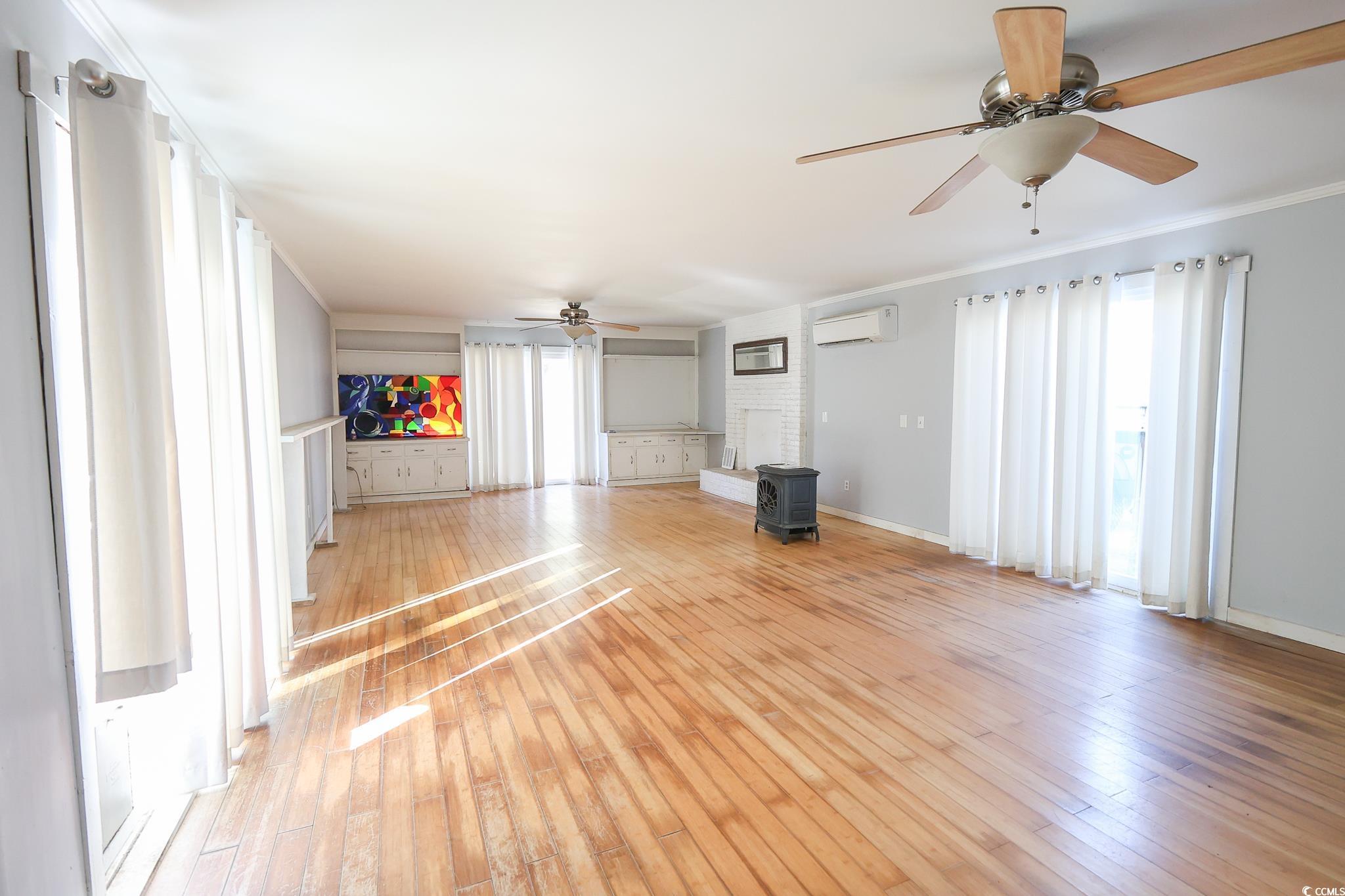 1841 Jasper Street Georgetown, SC 29440 - Photo 2 of 33 Unfurnished living room featuring crown molding, a wall mounted air conditioner, light hardwood / wood-style flooring, a wood stove, and ceiling fan