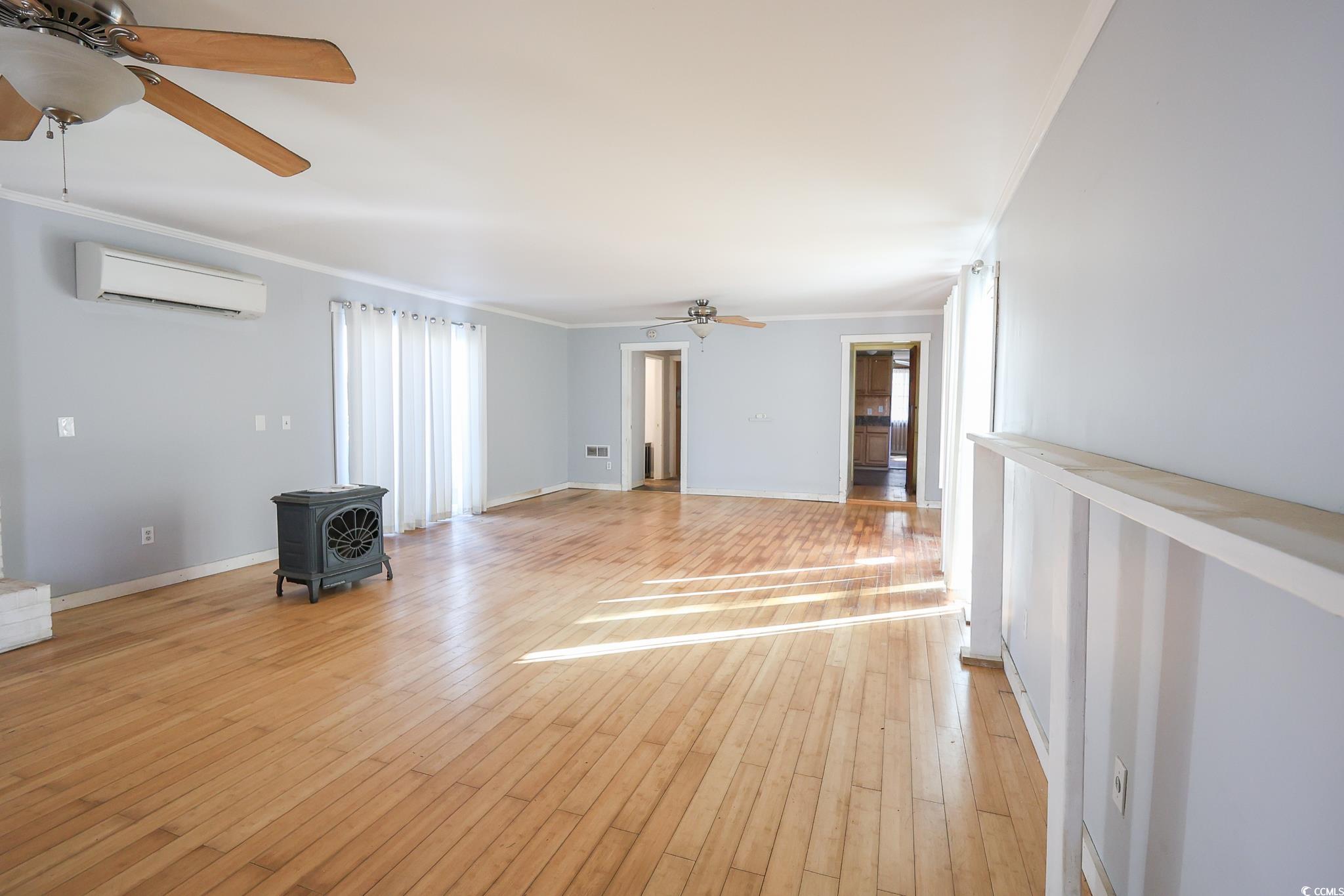 1841 Jasper Street Georgetown, SC 29440 - Photo 3 of 33 Unfurnished room with an AC wall unit, a wood stove, ceiling fan, crown molding, and light wood-type flooring