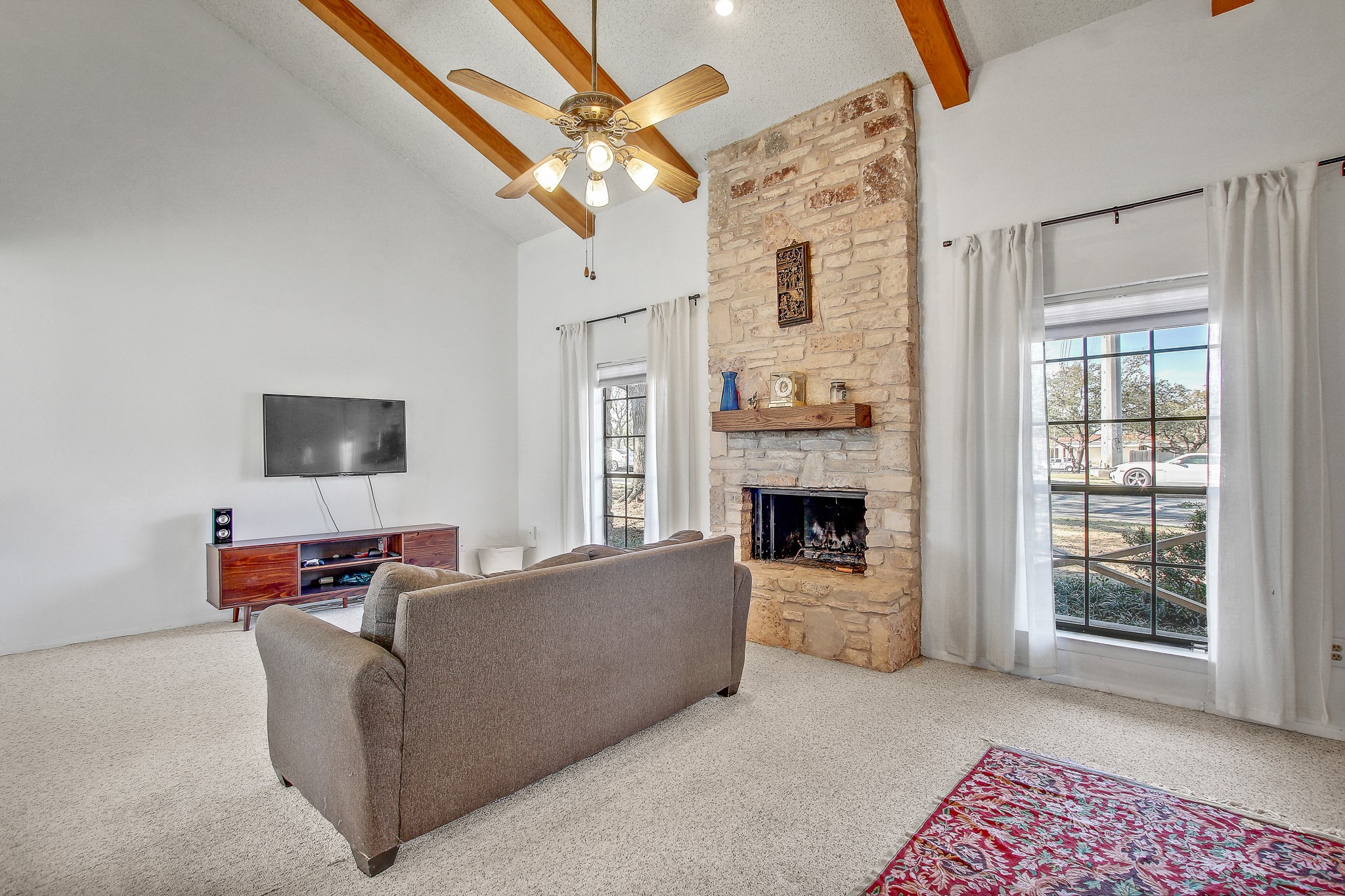 8925 North Plaza, Unit 69 Austin, TX 78753 - Photo 7 of 29 Carpeted living area featuring high vaulted ceiling, a stone fireplace, beam ceiling, and a ceiling fan